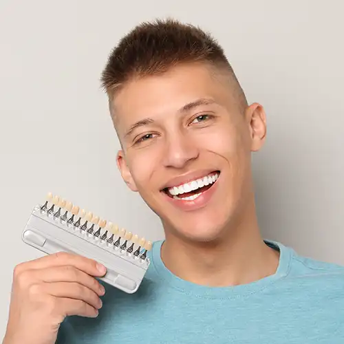 Young man smiling with porcelain veneer options in his hand from a cosmetic dentistry clinic.